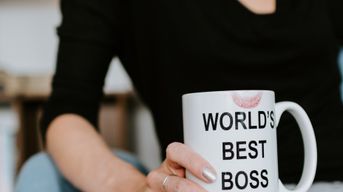 Woman from the waist down holding a coffee cup that says 'world's best boss' with a lipstick stain on the rim.