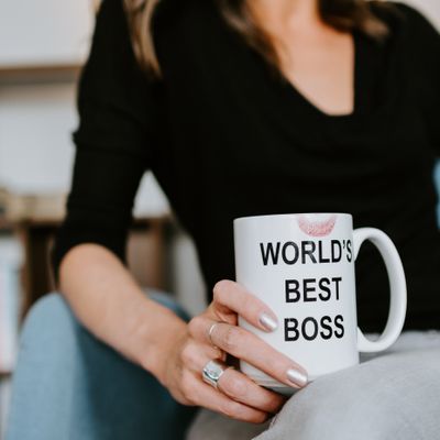 Woman from the waist down holding a coffee cup that says 'world's best boss' with a lipstick stain on the rim.